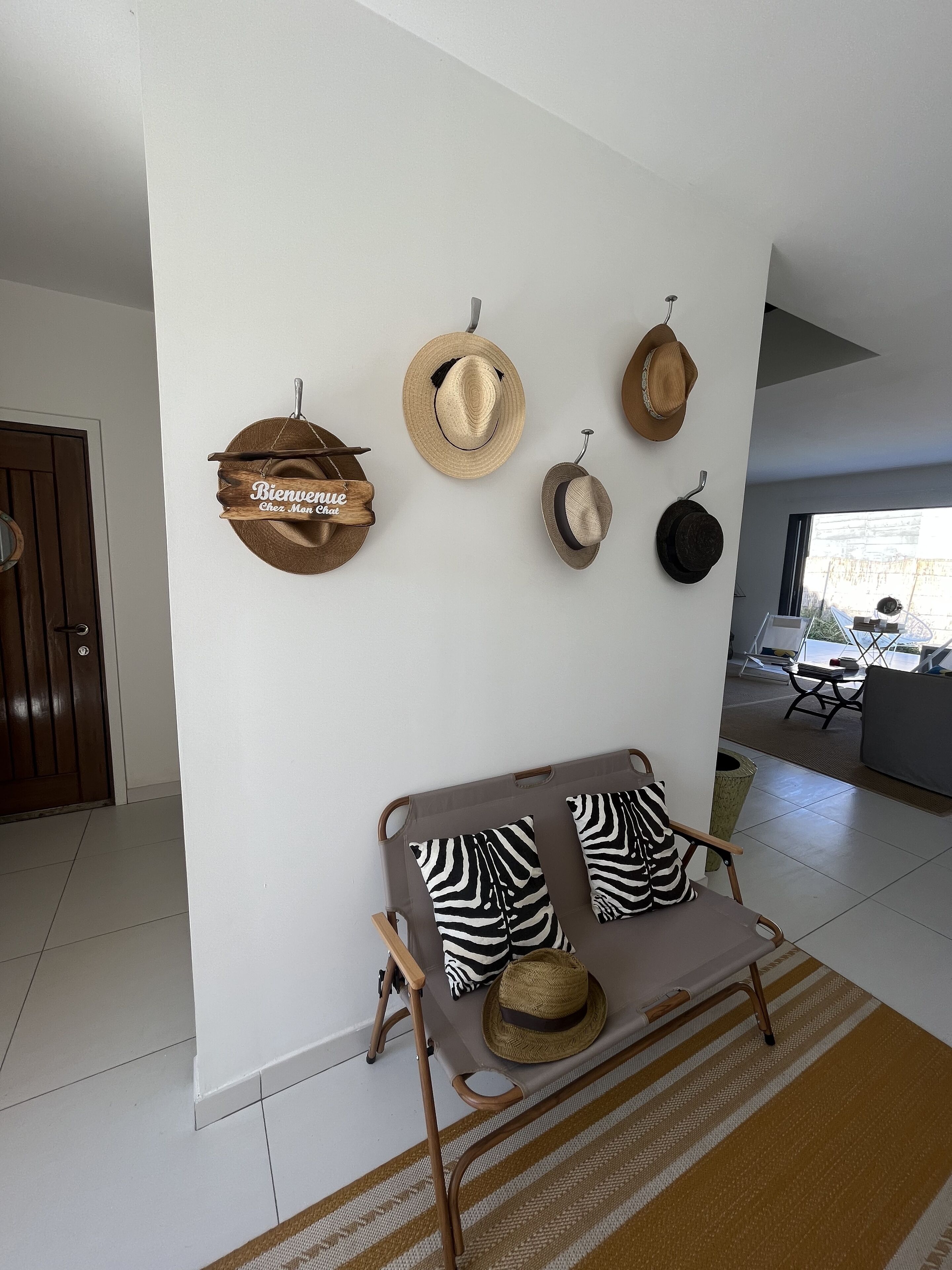 Un salon avec un canapé, deux coussins à motifs zébrés et un chapeau en fibres tressées posé sur une petite table.