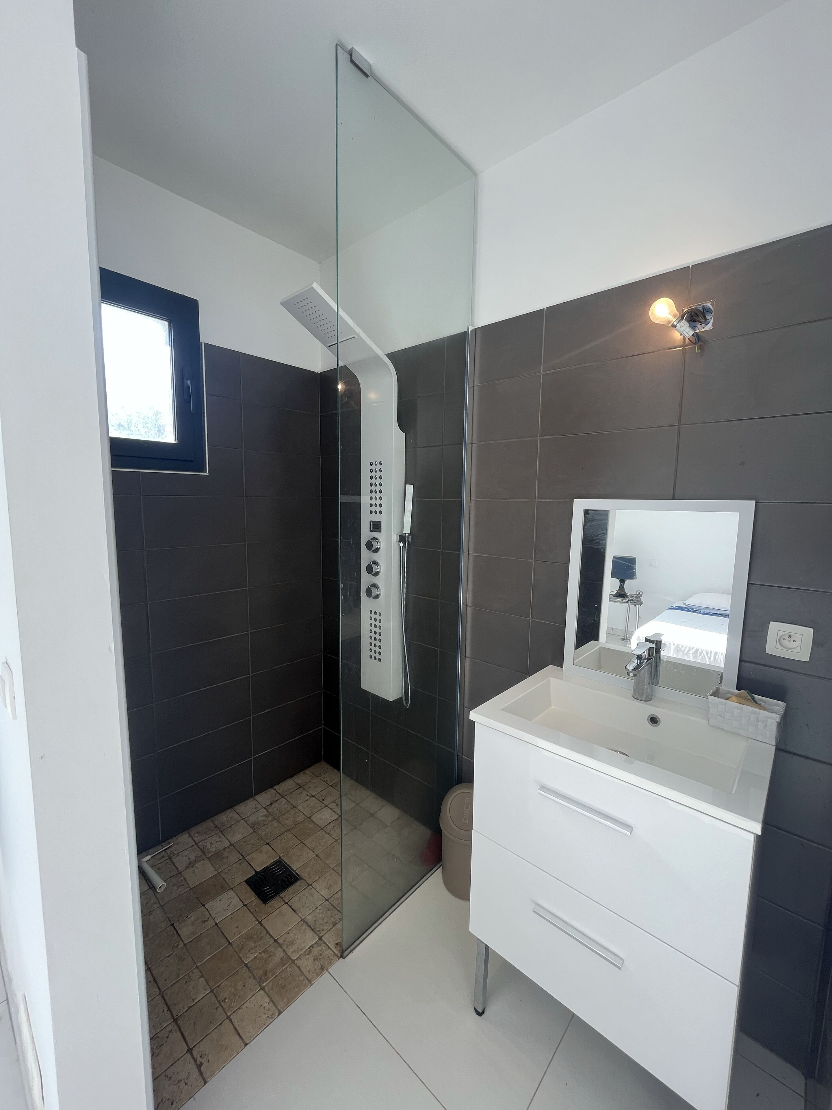 A modern bathroom with a glass-enclosed shower, a white vanity, and a large mirror.