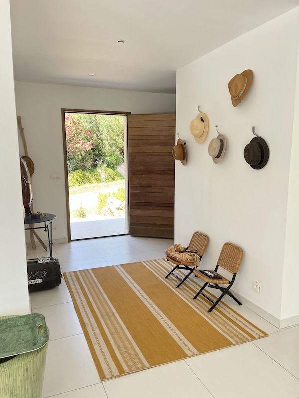 A modern living room with a large sliding glass door leading to a garden, two wicker chairs, a patterned rug, and a wall-mounted hat rack.