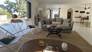 Un salón amplio con un gran ventanal, una mesa redonda con una revista, un sofá y una zona de comedor al fondo.