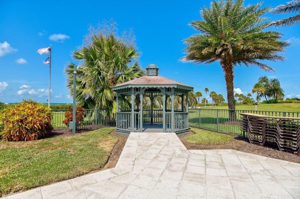 A gazebo with a tiled pathway leading to it, surrounded by palm trees and a flagpole.