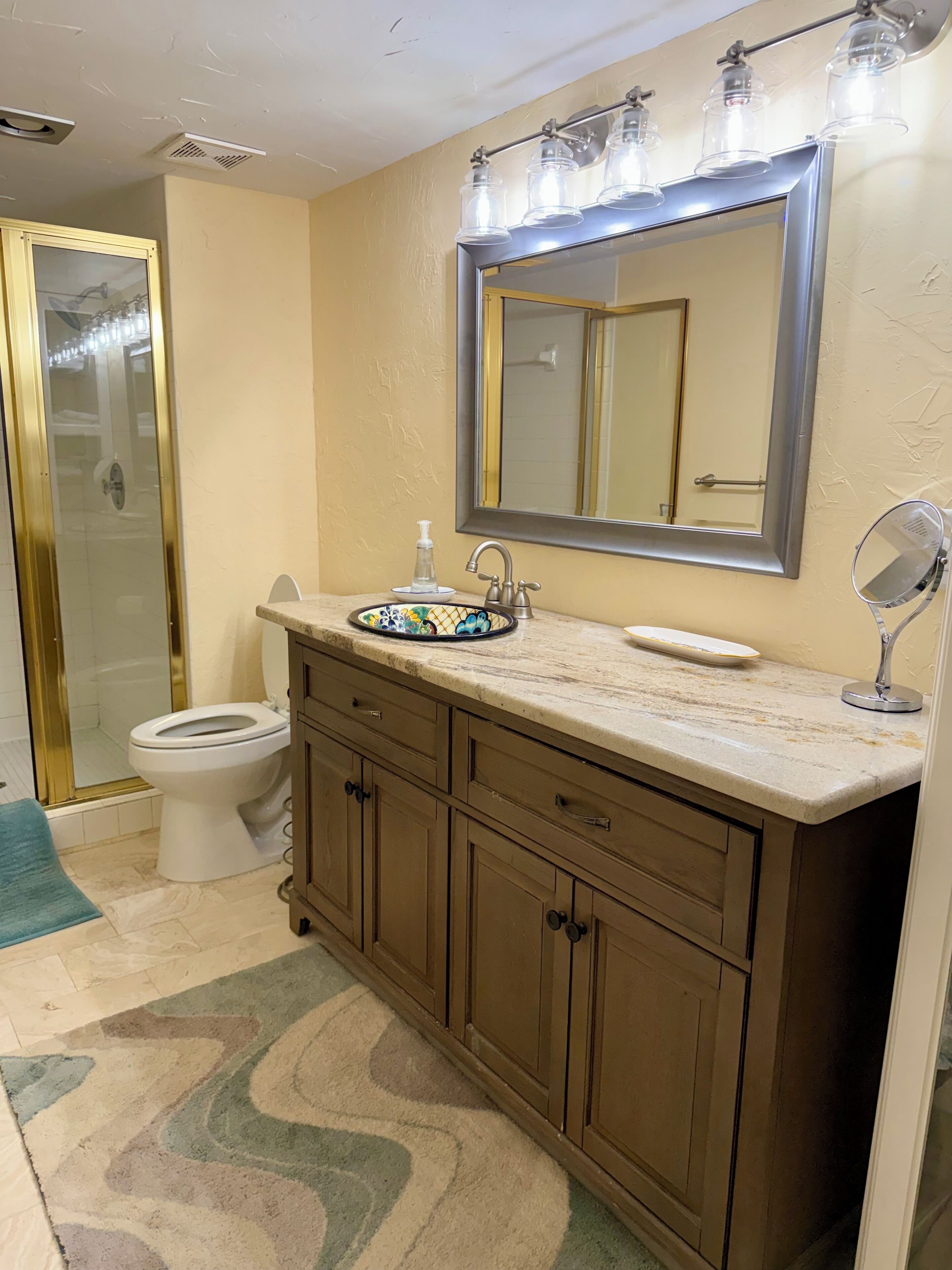 A bathroom with a toilet, sink, vanity, mirror, and shower.