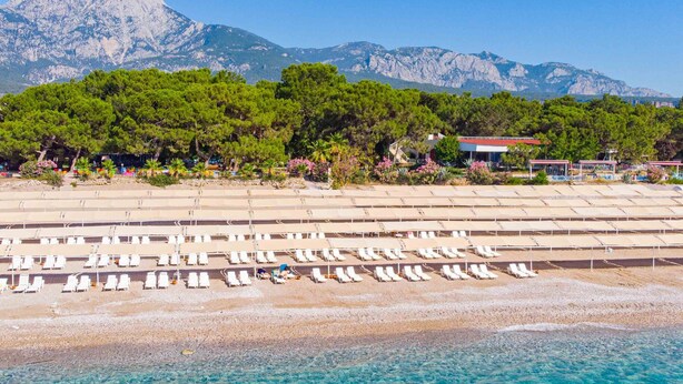 A beach with rows of sun loungers and a mountain in the background. - Tekirova Dora Butik Otel  (Kemer)