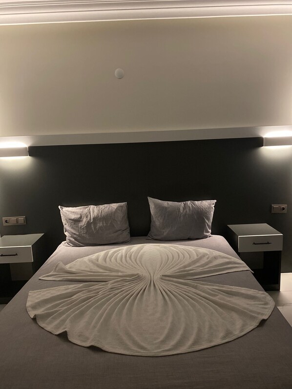 A neatly made bed with a circular patterned bedspread, two bedside tables, and a wall-mounted light fixture above the bed. - Tekirova Dora Butik Otel (Kemer)