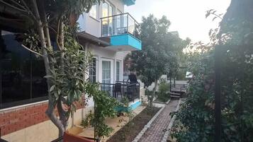 A two-story building with a balcony, surrounded by greenery and a paved pathway.