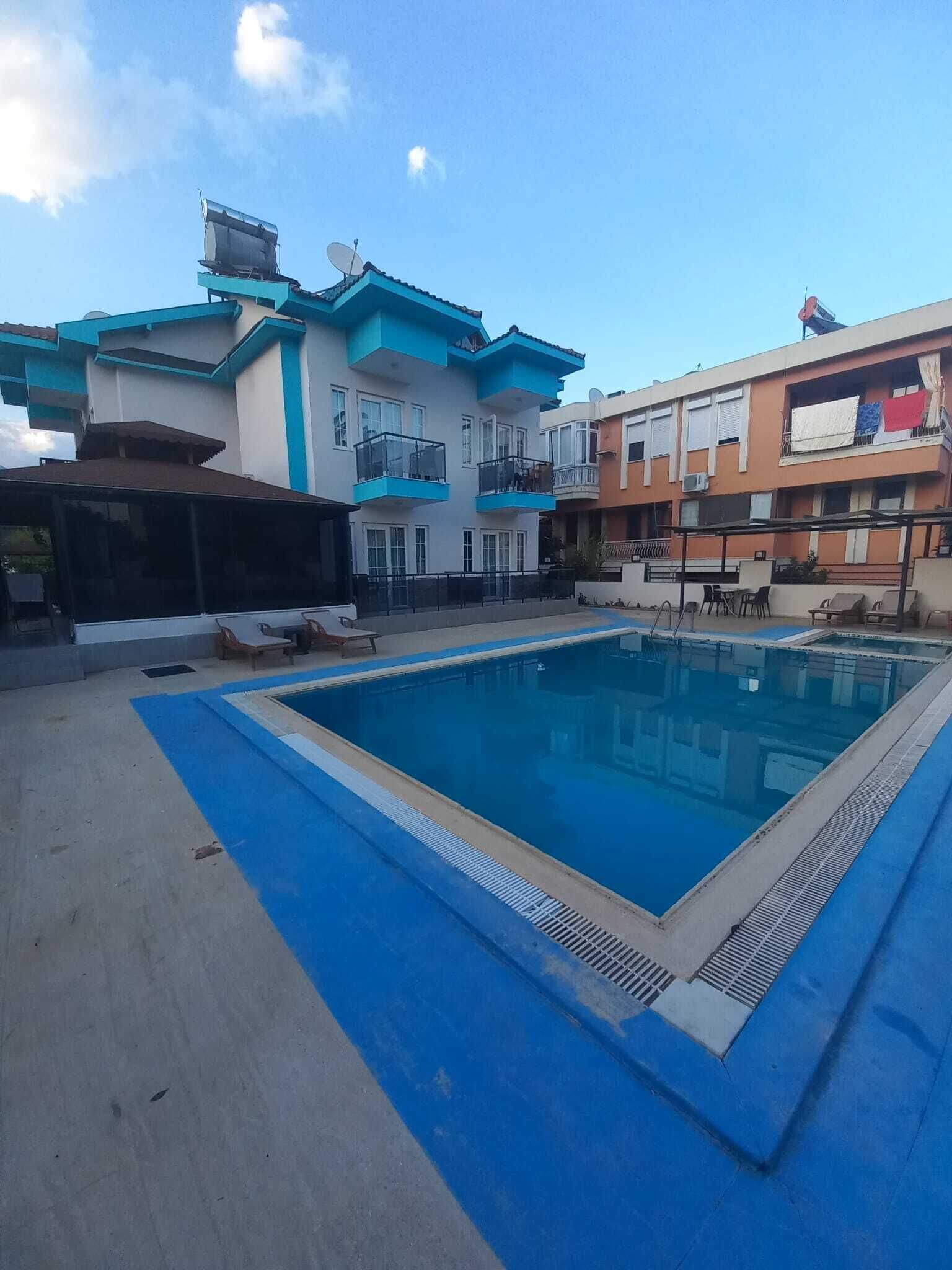 Une piscine bordée de bleu, entourée d’immeubles dotés de balcons et d’espaces de détente en plein air.