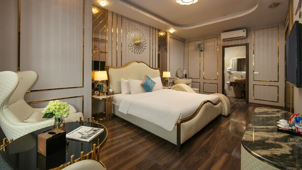 A spacious bedroom with a large bed, a sitting area with a table and chairs, and a vanity with a mirror. - BAO NGOC HOTEL LINH DAM (Hanoi)
