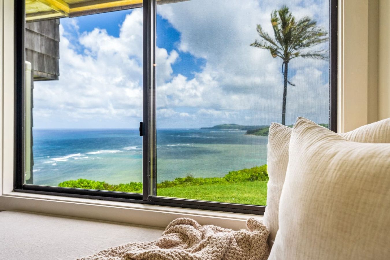 A room with a large window offering a view of the ocean and a tree.