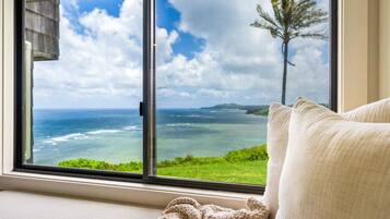 A room with a large window offering a view of the ocean and a tree.