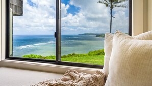 Ein Zimmer mit einem großen Fenster und Blick auf das Meer und einen Baum.
