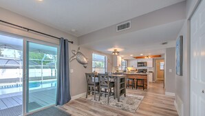 A spacious kitchen with a central island, a dining area with a table and chairs, and a sliding glass door leading to a pool area. - Nautical Nook Pool Home (Brandon)