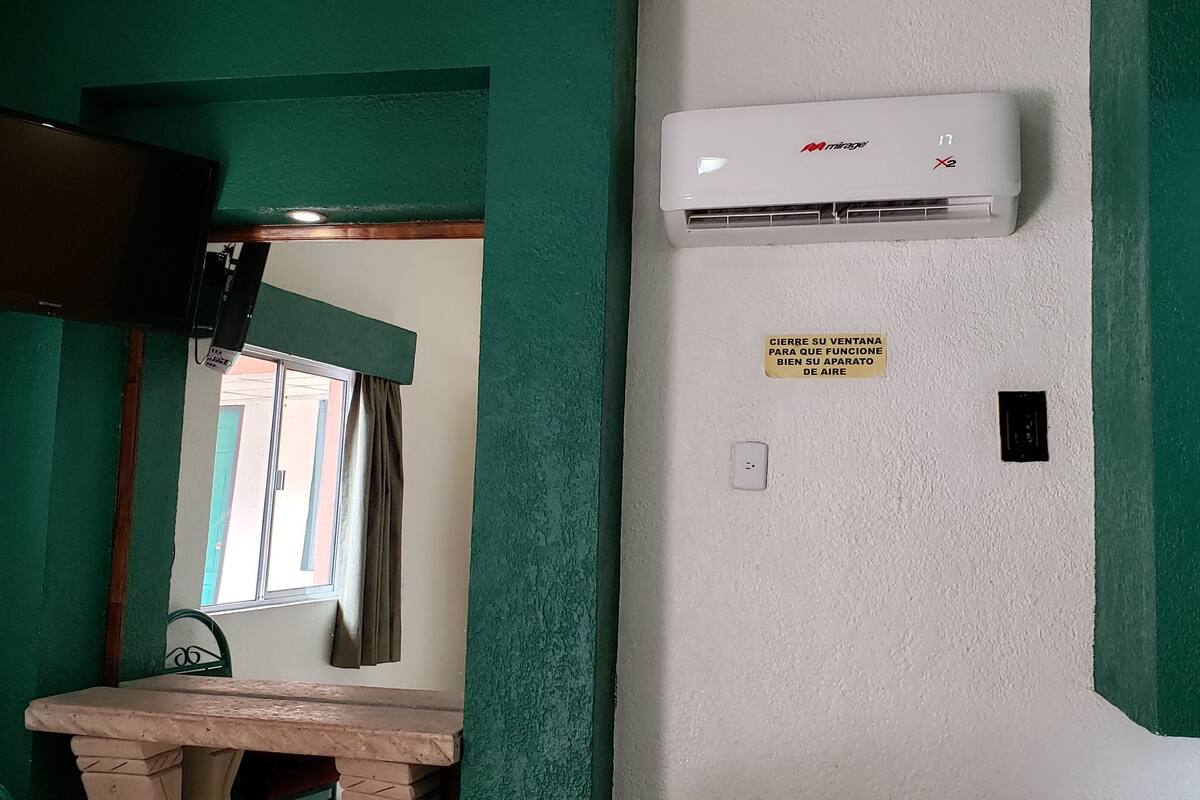 A room with a green wall, a mounted TV, an air conditioning unit, and a sign instructing to close the window for air conditioning.