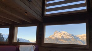 Una habitación con techo de madera, sofá púrpura y grandes ventanales con vistas a la montaña.