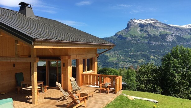 Una cabaña de madera con terraza, mobiliario exterior y vista a la montaña.