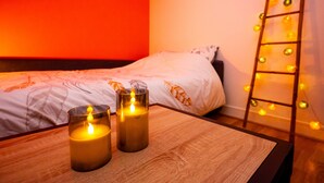 Un dormitorio con una cama, dos velas sobre una mesa de madera y una escalera con luces.