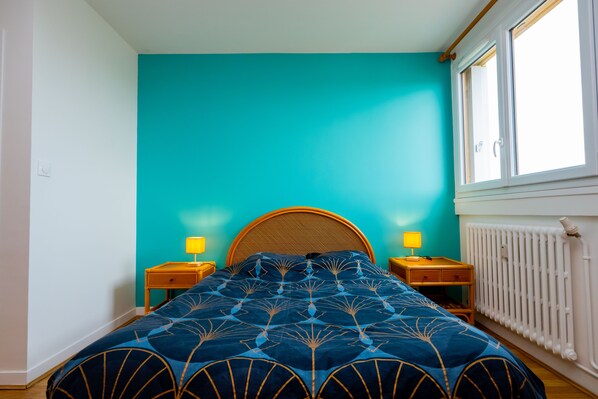 A bedroom with a teal wall, a wooden headboard, two bedside tables with lamps, and a radiator.