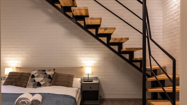 A bedroom with a bed, two nightstands, a lamp, a wooden staircase, and a white brick wall. - Eclectic and Design Duplex in the Heart of Prague by EasyBNB Premium (Prague)