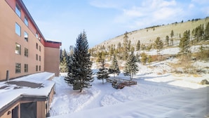 Zona exterior nevada con un edificio, árboles y una terraza de madera.