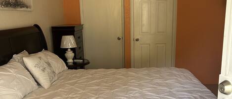 A bedroom with a large bed, two doors, a nightstand, a lamp, and a small rug.
