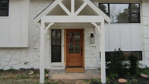 Une maison avec une façade en pierre, une porte d’entrée en bois et un petit porche doté d’une balustrade blanche.