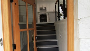 Une porte en bois donne sur un escalier, avec un coin cuisine visible au fond.