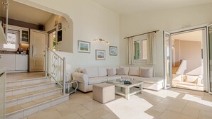 A spacious living area with a sofa, coffee table, and a staircase leading to a kitchen. - Kalami Beach - Villa Kouloura (Corfu)