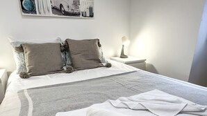 A neatly made bed with a grey and white striped blanket, two pillows, and two rolled white towels on a white mattress.
