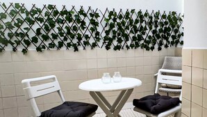 A small room with two white chairs and a white table, a tiled floor, and a wall decorated with green ivy.