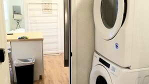 Un lavadero con dos lavadoras apiladas, un pequeño cubo de basura y suelo de madera.