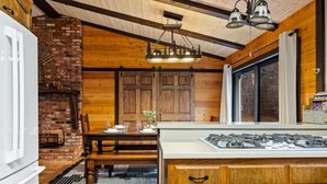 A rustic kitchen with a brick fireplace, wooden ceiling beams, and a modern gas stove. - Ritz-Craterton|Spa + BBQ + Game Room + EV + Pups (Big Bear Lake)