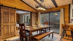 A wooden dining room with a large table set for four, a bench, and a bar area with stools. - Ritz-Craterton|Spa + BBQ + Game Room + EV + Pups (Big Bear Lake)