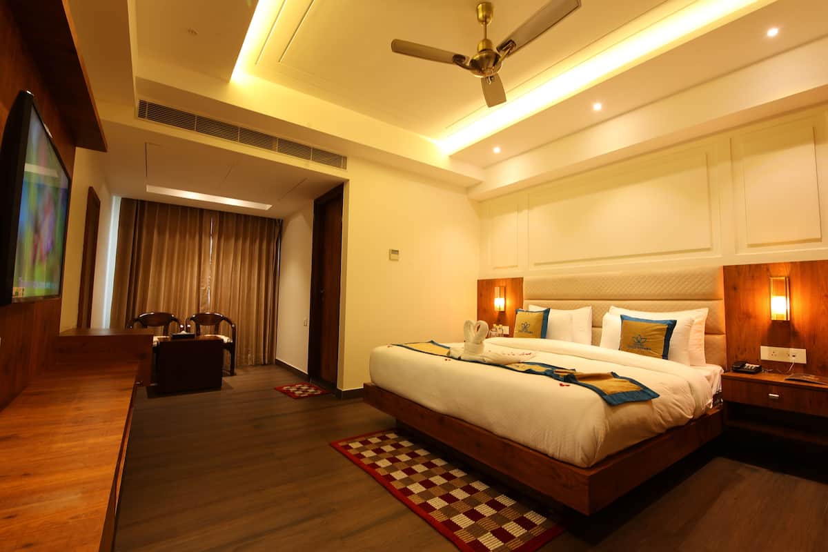 A hotel room with a large bed, wooden floor, ceiling fan, and a TV on the left wall.