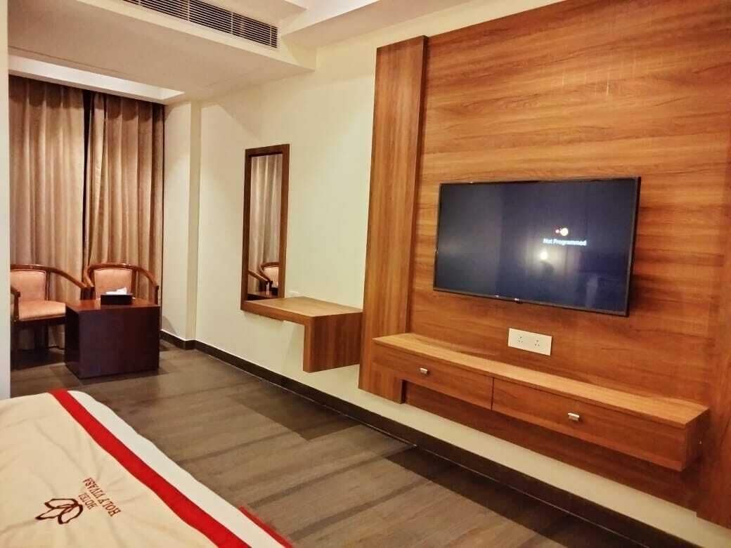 A hotel room with a large flat-screen TV mounted on a wooden wall, a bed with a red and white striped bedspread, a small wooden side table, and a chair.