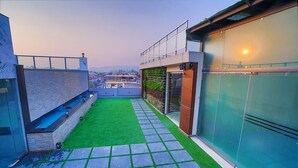 A rooftop terrace with a green lawn, a stone pathway, and a glass wall. - HOLY VIVASA  (Rishikesh)