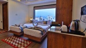 A hotel room with two beds, a large window, a wooden desk with a kettle, and a red and beige rug. - HOLY VIVASA  (Rishikesh)