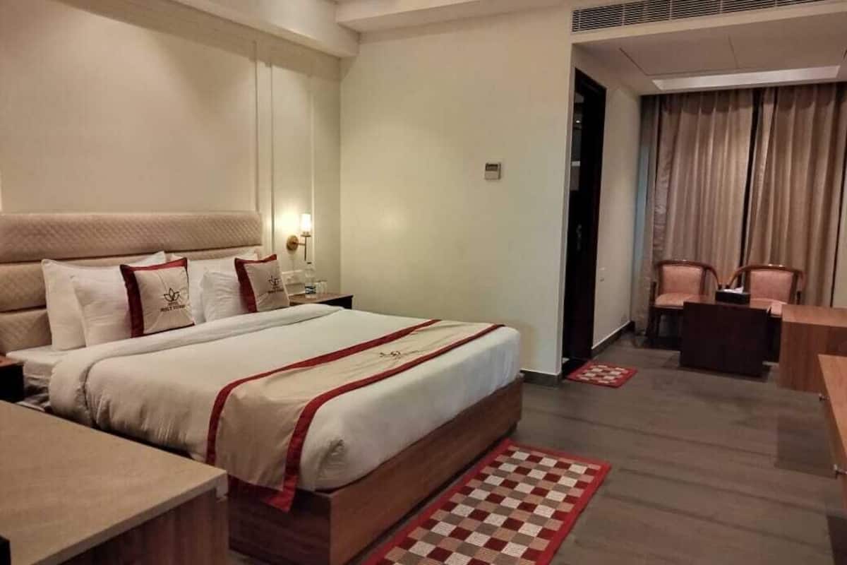 A hotel room with a large bed, a desk, and a chair. There is a door leading to another room.
