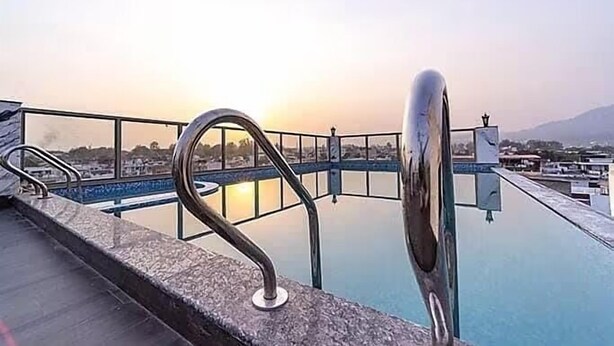 A rooftop pool with a metal railing and a view of the cityscape at sunset. - HOLY VIVASA  (Rishikesh)