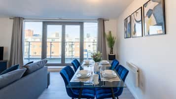 A modern dining area with a glass table, blue chairs, and a grey sofa.