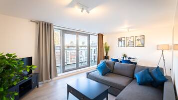 A modern living room with a sofa, coffee table, TV, and large windows.