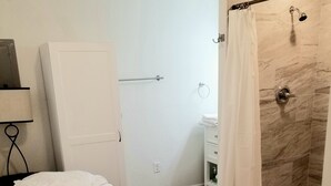 Ein Hotelzimmer mit Bett, Duschbereich mit Marmorwand und einem kleinen Nachttisch mit Lampe.