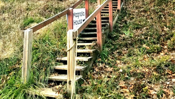 Eine Holztreppe führt zu einem Haus mit der Aufschrift 'Magnolia House'.