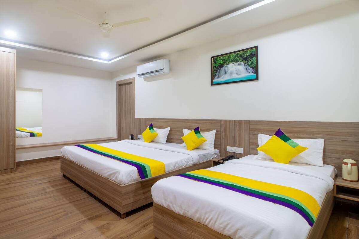 A hotel room with two beds, wooden flooring, a ceiling fan, an air conditioning unit, and a framed picture on the wall.