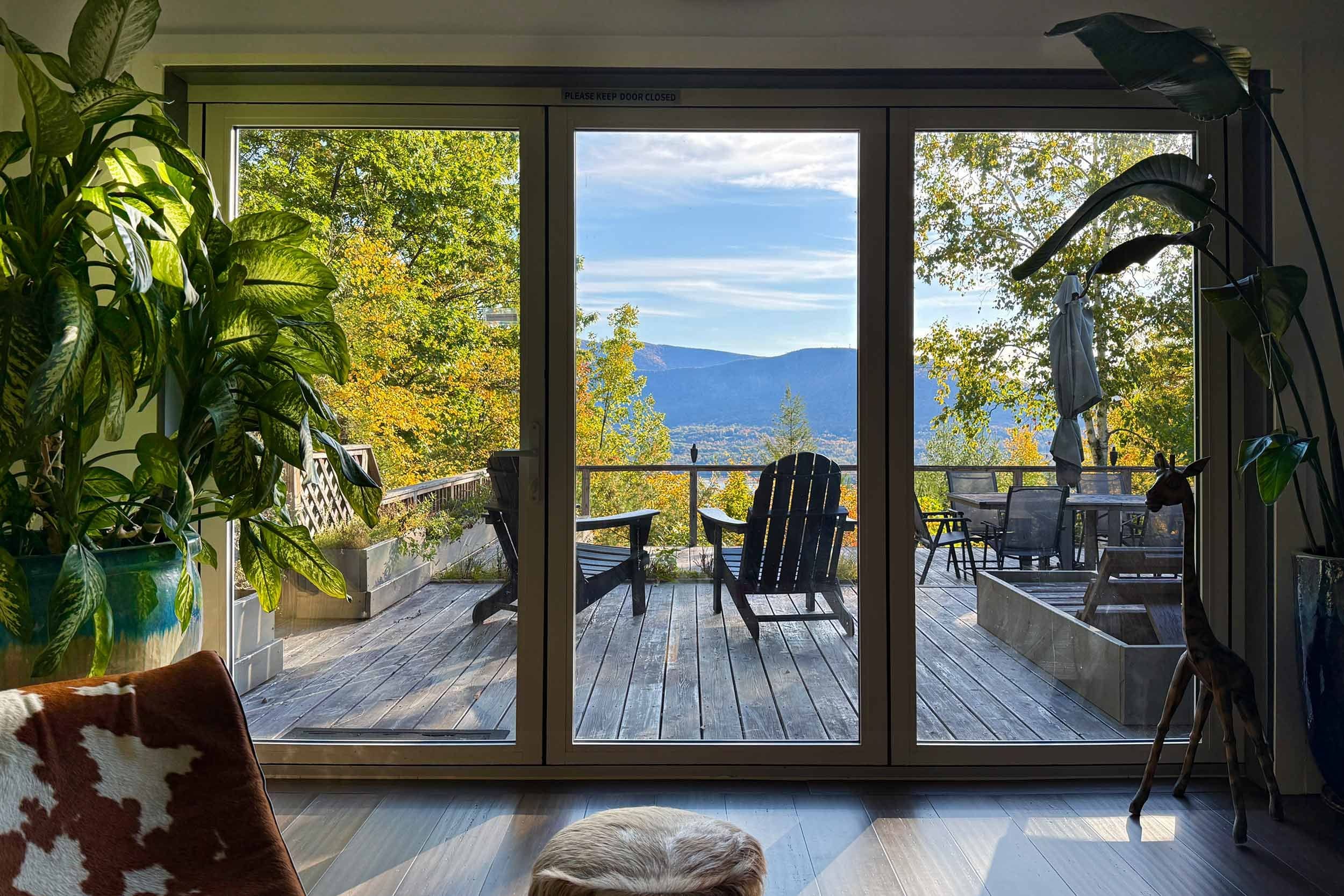 Una habitación con puerta corrediza de vidrio que da a una terraza exterior con vistas a árboles y montañas.
