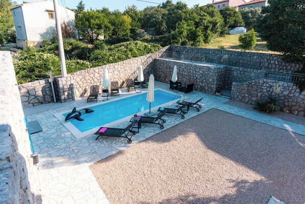 A swimming pool with lounge chairs and umbrellas, surrounded by stone walls and greenery.
