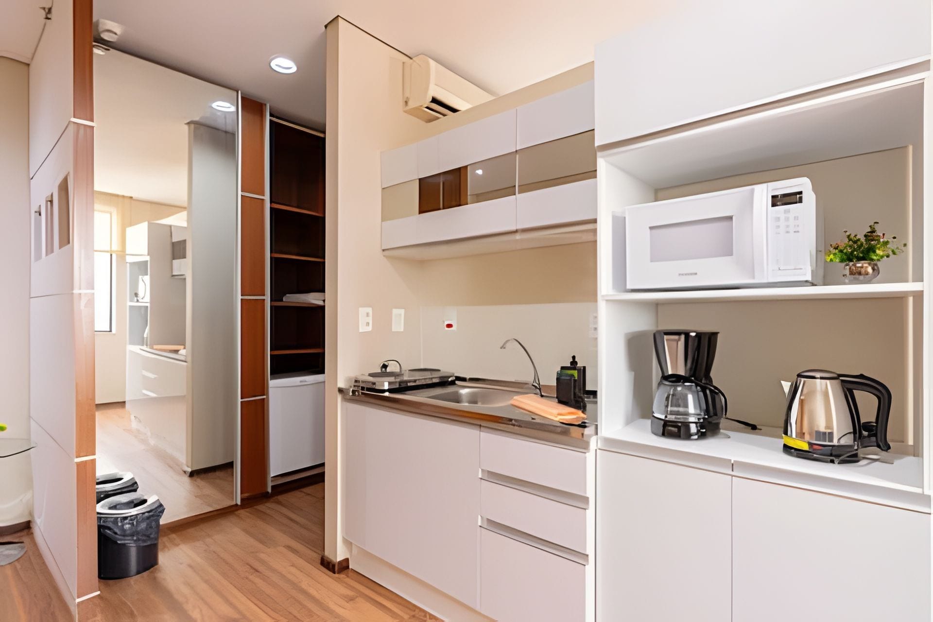 A modern kitchen with white cabinets, a built-in microwave, a coffee maker, and a sink.