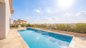 Uma piscina com bordas azulejadas, um deck de pedra e vista para edifícios ao fundo.