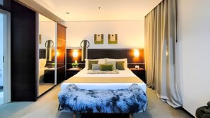 A modern hotel room with a large bed, a mirror, two bedside tables with lamps, a wardrobe, and a sliding door.
