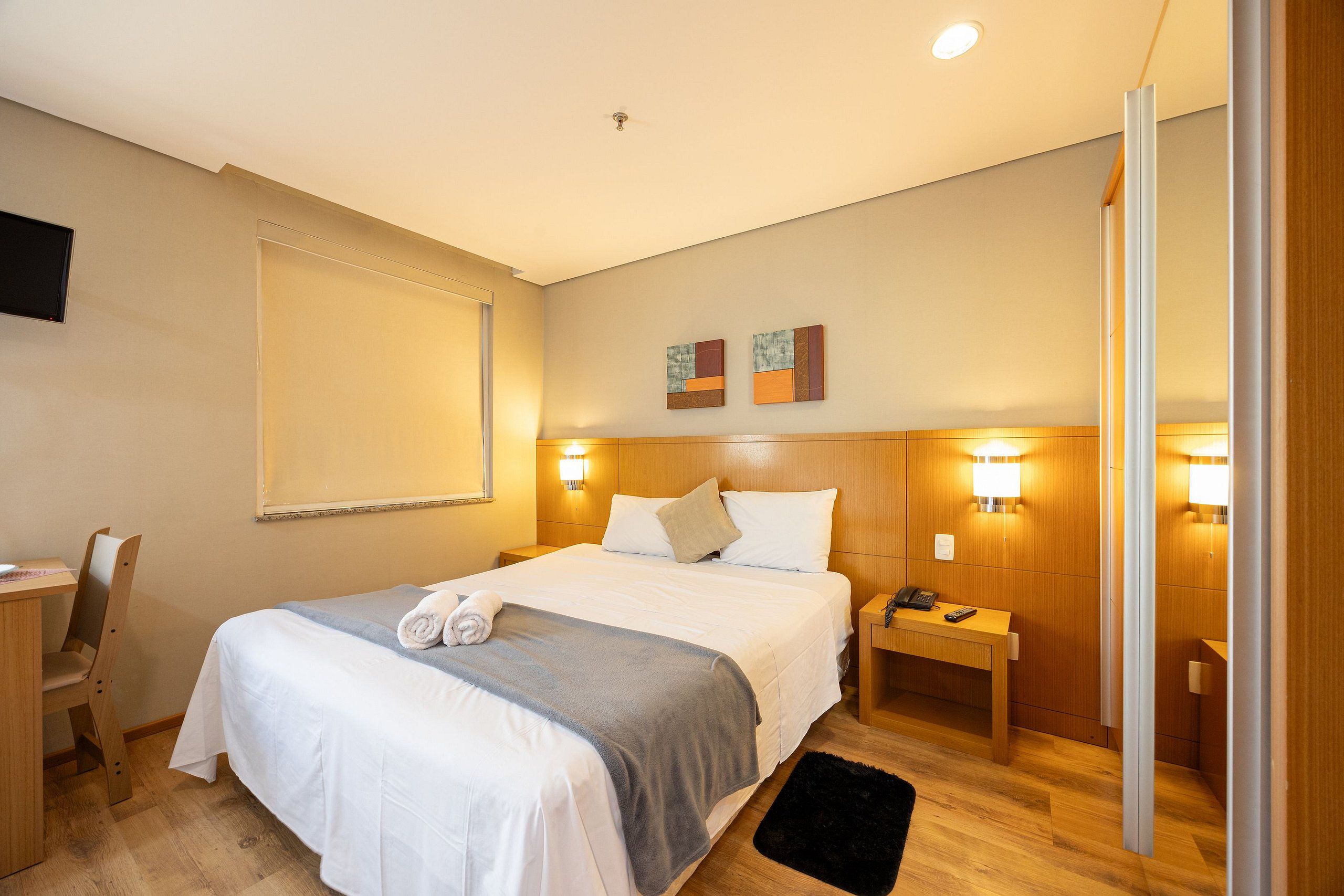 A hotel room with a bed, bedside tables, a desk, and a chair.