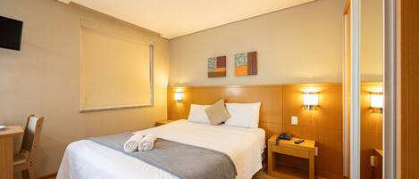 A hotel room with a bed, bedside tables, a desk, and a chair.