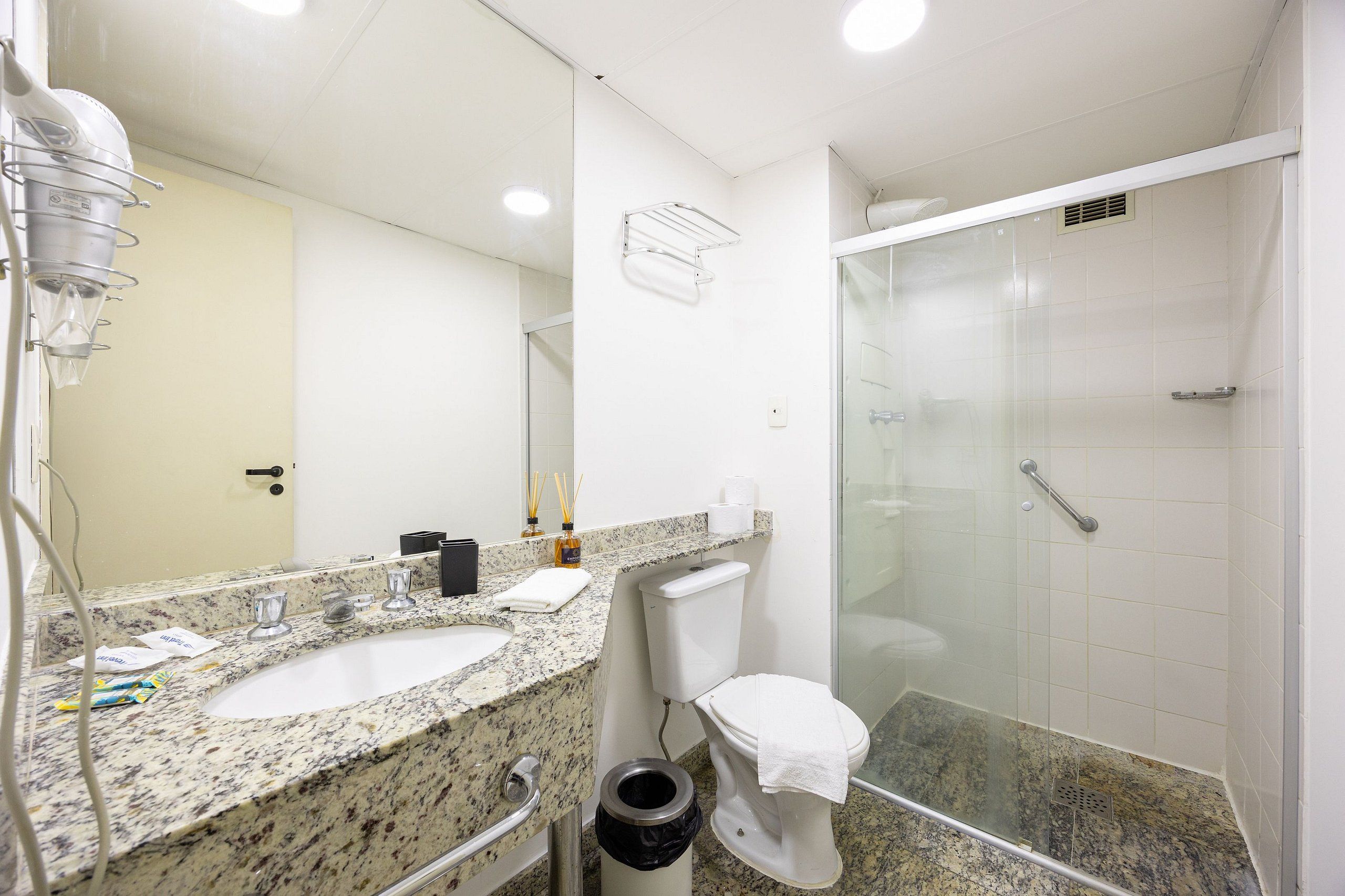 A bathroom with a granite countertop sink, a white toilet, a glass shower enclosure, and a towel rack.